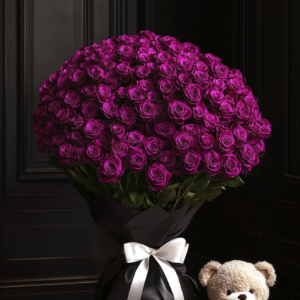 A luxurious bouquet of fuchsia roses wrapped in black satin with a white ribbon, accompanied by a plush teddy bear.