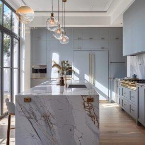 A modern kitchen with blue cabinetry and a marble island featuring a gold faucet and pendant lights.