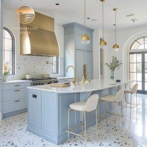 A modern kitchen with a golden range hood, blue cabinets, and a marble island with gold accents.